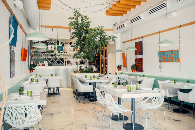 Bright modern café interior with an indoor tree, mint-green banquette seating, white tables, pendant lamps and colorful wall art