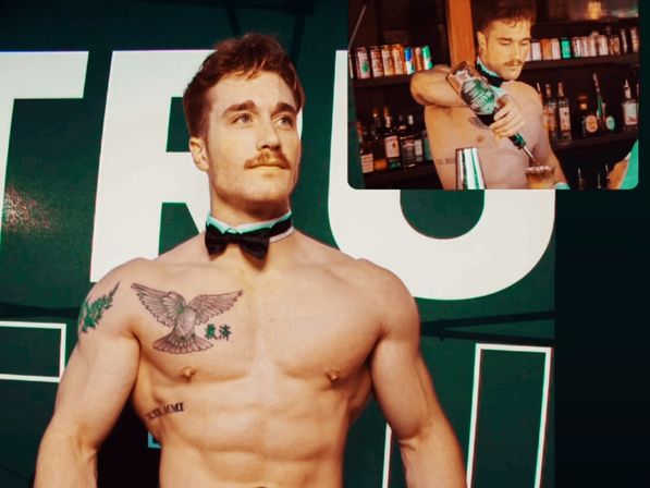 Shirtless muscular male bartender in black bow tie and collar with chest tattoos posing against a green event backdrop, inset photo shows him pouring a cocktail behind a bar.