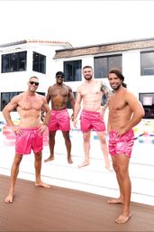Four shirtless men in bright pink swim trunks striking playful poses poolside at a sleek white coastal house with colorful inflatable floats.