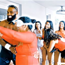 Lively bachelorette party in a bright modern home — a blindfolded guest hugs a laughing man while bridesmaids in orange and a woman in white cheer.
