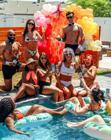 Backyard summer pool party: adults in swimsuits and sunglasses toasting drinks by a pool and colorful balloon arch, floating on inflatable loungers on a sunny day