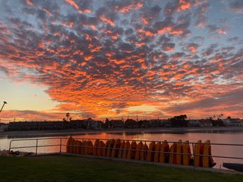 Dramatic orange sunset and cloudscape over a coastal lagoon with stacked yellow kayaks and silhouetted waterfront homes