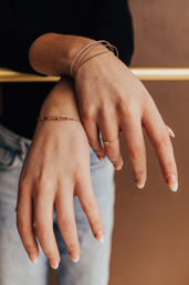 Close-up of hands wearing thin gold bracelets and a delicate gold ring, French-tip manicure, casual denim and neutral background — lifestyle jewelry fashion shot