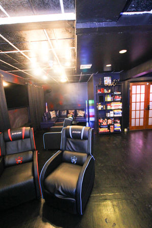 Basement home theater and gaming lounge with black leather recliner chairs, colorful LED accent lights, a cozy sofa and shelf of board games