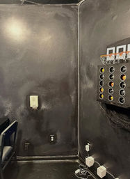 Home game-room corner with matte black walls, mounted mini basketball toss holding orange balls, visible outlets and charging cords.