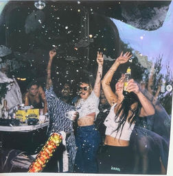 Festive indoor party scene with people dancing under a disco ball as confetti falls, hands raised and drinks in hand — lively nightlife celebration.
