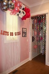 Playful pink girls room entryway decorated for a party with metallic and cow-print balloon garland, iridescent fringe window curtain, hanging sequin bead doorway, and glitter LETS GO GIRLS banner.