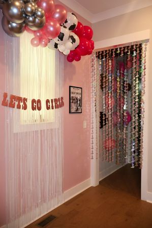 Playful pink girls room entryway decorated for a party with metallic and cow-print balloon garland, iridescent fringe window curtain, hanging sequin bead doorway, and glitter LETS GO GIRLS banner.