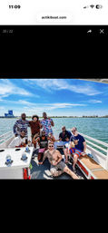Eight friends posing on a sunny party boat cruising a calm blue bay with a clear sky and distant coastline