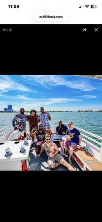 Eight friends posing on a sunny party boat cruising a calm blue bay with a clear sky and distant coastline