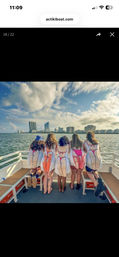 Five friends on a boat deck facing a coastal city skyline, wearing novelty towels printed like bikini backs during a sunny, partly cloudy cruise.