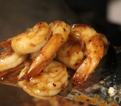 Close-up of golden-brown, seasoned sautéed shrimp glazed in a garlic-butter sauce resting on a metal spatula over a hot pan