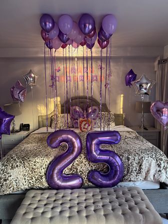 Purple-themed bedroom birthday surprise with floating lavender and plum balloons, star and heart foil balloons, a 'Happy Birthday' banner and large metallic '25' number balloons on a leopard-print bed.