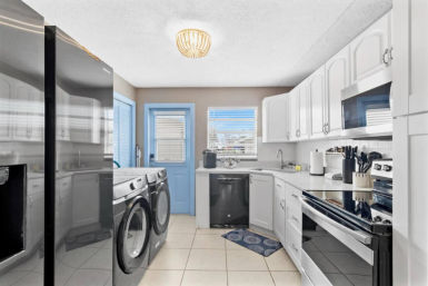 Bright modern kitchen-laundry combo in a home with white cabinets, stainless appliances, front-loading washer and dryer, blue back door and tiled floor