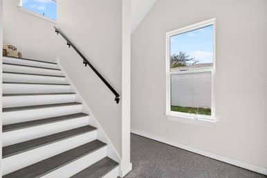 Bright modern entry with gray wood-tread staircase and black handrail, white walls, carpeted landing and window overlooking a backyard.