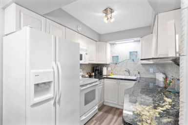Bright white U-shaped condo kitchen with dark granite countertop, white appliances, sink, and coastal wall art