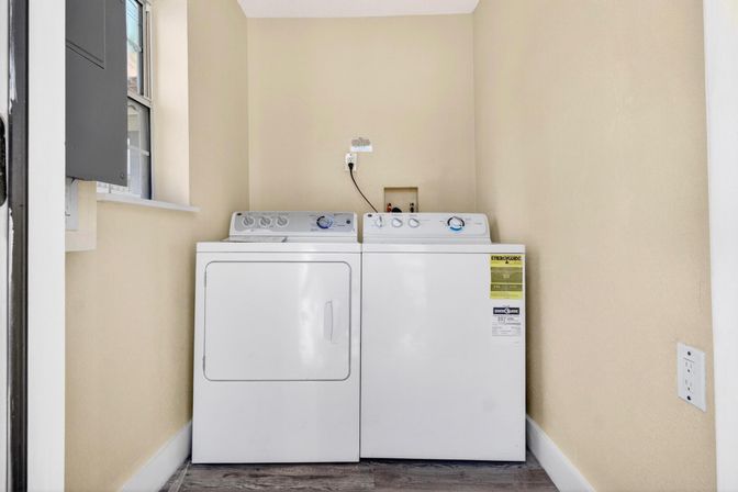 Cozy laundry nook with white side-by-side washer and dryer against beige walls, wood-look flooring and a small window.