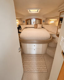 Cozy beige yacht stateroom with rounded queen bed, porthole windows, overhead hatch, built-in drawers and warm wood trim
