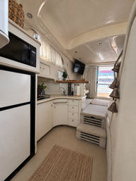 Bright beige yacht interior with compact galley—microwave, fridge, sink and curved cabinetry—carpeted steps up to the cockpit and a sliding door revealing docked boats.