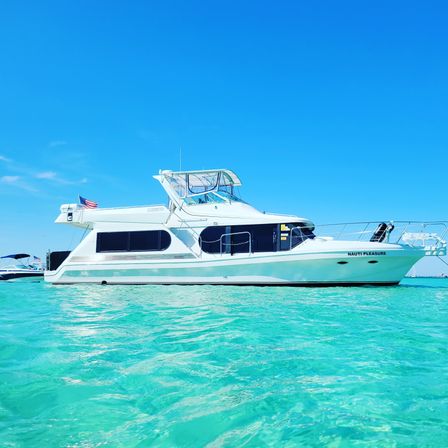 Sleek white motor yacht floating in crystal-clear turquoise water beneath a bright blue sky — sunny tropical boating and vacation vibes.