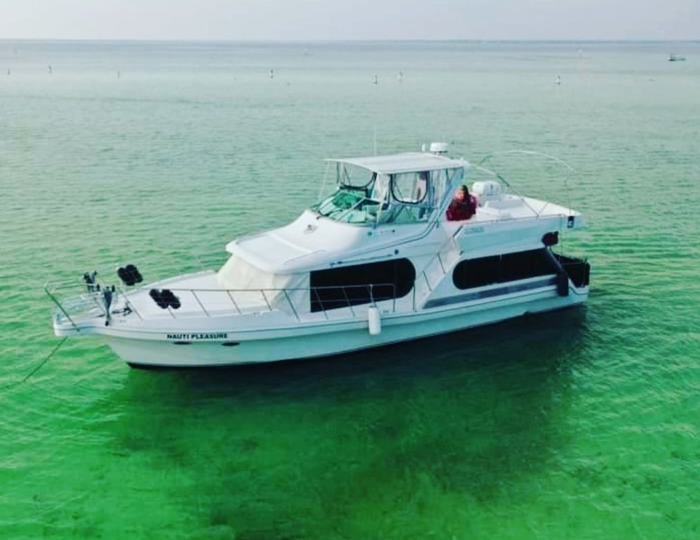 Aerial shot of a white cabin cruiser motor yacht drifting in clear emerald-green coastal water on a sunny day