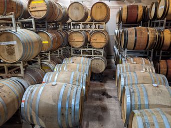 Rustic winery cellar with rows of oak aging barrels bound by metal hoops, stacked on racks and lined along a concrete floor