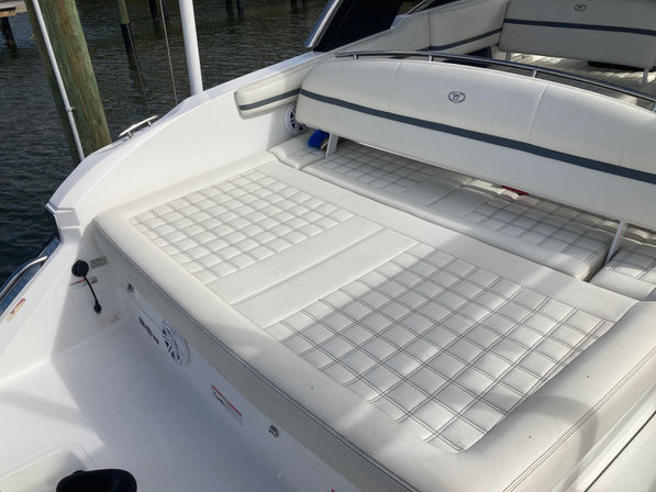 White quilted vinyl sun pad with fold-up backrest on a yacht stern, docked at a marina with wooden pilings and calm water — inviting lounging on the boat.