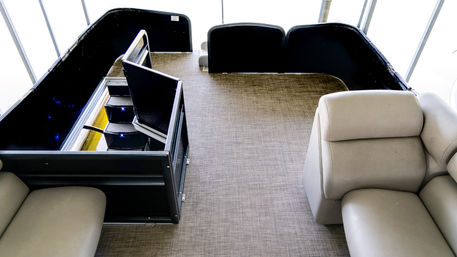 Pontoon boat interior with beige vinyl lounge seats, gray woven deck carpet, black railings and folded console panels