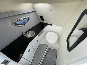 Compact marine head in a boat cabin with black countertop, stainless sink, white marine toilet, oval porthole, padded cream walls and mirrored door — small yacht bathroom.