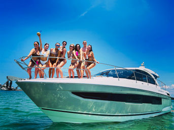 Group of women in bikinis posing on the bow of a white yacht over turquoise water under a bright blue sky — sunny yacht party.