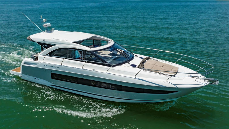 White luxury motor yacht cruising on calm emerald-green coastal waters, sleek glass cabin and cushioned bow sunpad.