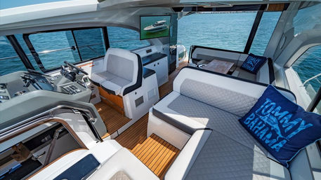 Sunlit luxury motor yacht cockpit and salon with white quilted seating, teak deck, helm station, small table and panoramic blue ocean views