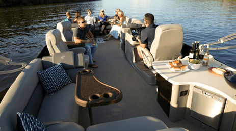 Group of friends relaxing on a pontoon boat on a calm lake with cushioned seating, helm, and a small bar area with snacks and wine for a scenic lake cruise