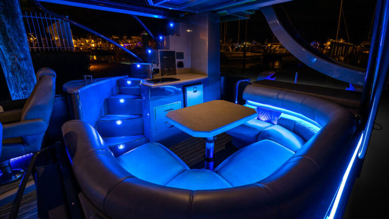 Glowing blue LED curved lounge and dining table on a luxury yacht docked at a marina at night