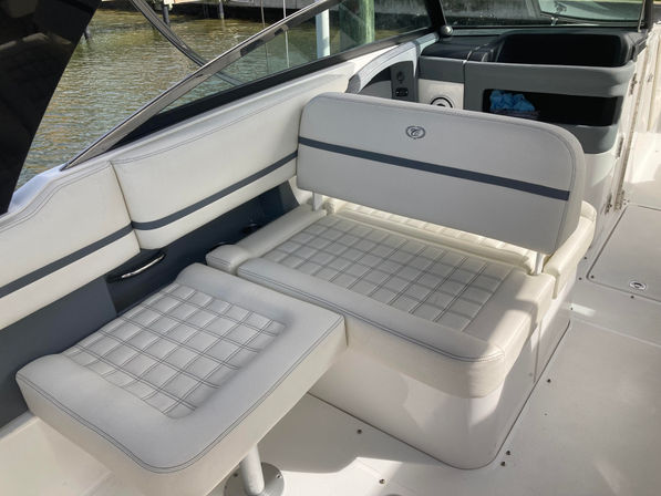 White marine cushioned bench and swivel seat with quilted stitching in a boat cockpit, sunlight on deck and calm marina water visible through the windshield
