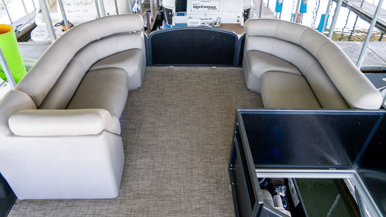 Inviting lounge-style beige curved bench seating on a pontoon boat deck with textured marine carpet, open center walkway and dockside marina view