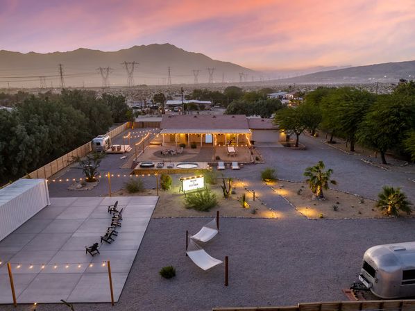 Cozy desert retreat at sunset with string-lit courtyard, Airstream trailer, hammocks, lounge chairs, hot tubs and mountain backdrop