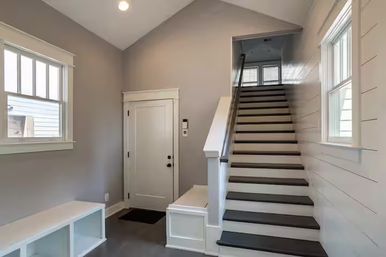 Bright modern home entryway with a straight staircase, white trim and shiplap wall, built-in bench with cubbies, neutral gray walls and windows letting in natural light.