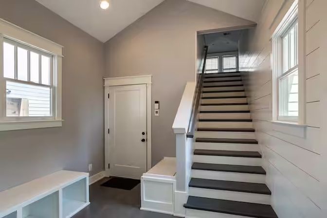 Bright modern home entryway with a straight staircase, white trim and shiplap wall, built-in bench with cubbies, neutral gray walls and windows letting in natural light.