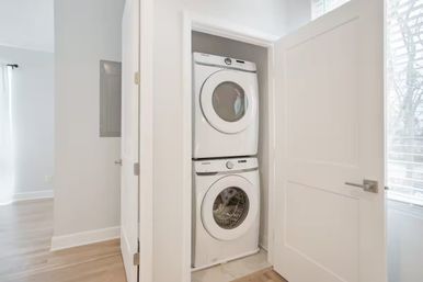 Bright modern apartment hallway with a white stacked washer and dryer tucked inside a closet — compact in‑unit laundry solution for small‑space living.
