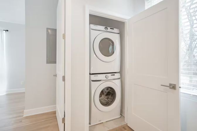 Bright modern apartment hallway with a white stacked washer and dryer tucked inside a closet — compact in‑unit laundry solution for small‑space living.