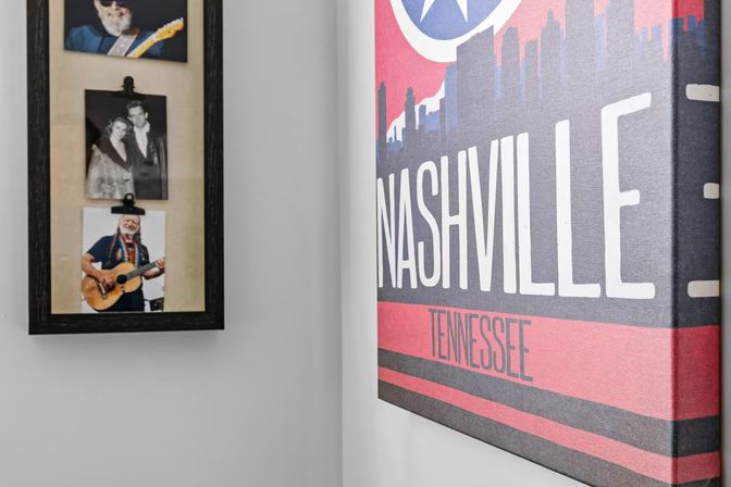 Music-themed wall with a colorful "Nashville, Tennessee" canvas print beside a black-framed collage of vintage musician photos on a white wall