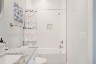Bright modern residential bathroom interior with white bathtub-shower, pastel striped shower curtain, marble vanity countertop and brushed nickel fixtures