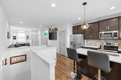Bright open-concept Nashville, TN apartment kitchen and living area with dark wood cabinets, stainless steel appliances, white island with two bar stools, hardwood floors and a decorative "Nashville" wall sign.