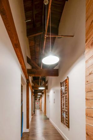 Cozy industrial-loft hallway with exposed wooden beams and ceiling pipes, hanging pendant lights, hardwood floor and framed wall display