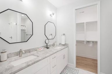 Bright modern master bathroom with white double vanity and marble countertop, black octagonal mirrors and open walk-in closet
