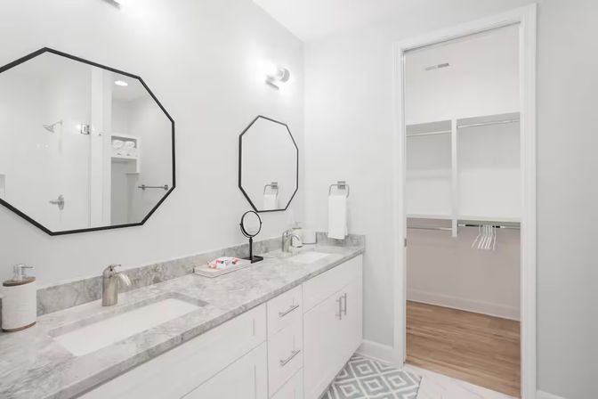 Bright modern master bathroom with white double vanity and marble countertop, black octagonal mirrors and open walk-in closet