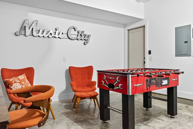 Cozy Nashville game room with a red foosball table, retro orange lounge chairs and a metal 'Music City' wall sign.