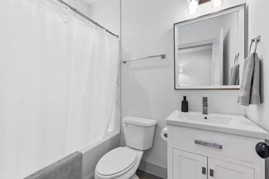 Crisp modern white bathroom interior with tub and shower curtain, toilet, white vanity and sink, mirror, chrome fixtures and gray towels.