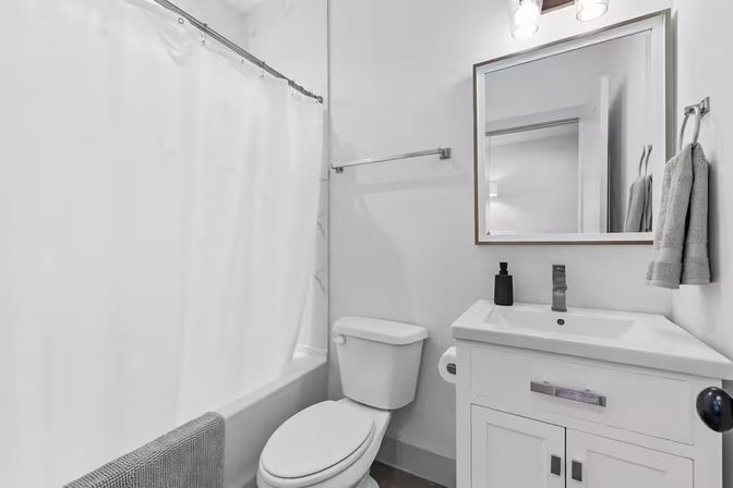 Crisp modern white bathroom interior with tub and shower curtain, toilet, white vanity and sink, mirror, chrome fixtures and gray towels.